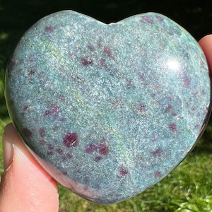 May include: A heart-shaped green and red ruby zoisite crystal. The crystal has a smooth, polished surface and is speckled with red ruby inclusions.