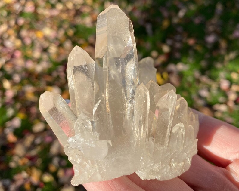 Puede incluir: Un c&uacute;mulo de cristales de cuarzo transparentes de diferentes tama&ntilde;os y formas. Los cristales est&aacute;n dispuestos en un c&uacute;mulo, con algunos de los cristales apuntando hacia arriba y otros hacia abajo. Los cristales son transl&uacute;cidos y tienen un ligero brillo.