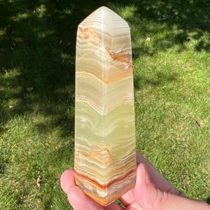 May include: A green and brown onyx obelisk with a pointed top. The obelisk has a layered pattern of green, brown, and white.