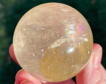 Op de afbeelding: Een heldere, iriserende, gouden bol van kristal. De bol heeft een lichtgouden tint en vertoont regenboogkleurige irisatie.