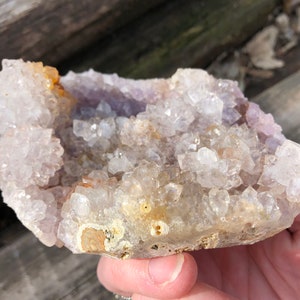 K&ouml;nnte beinhalten: Ein Cluster aus klaren Quarzkristallen mit einem violetten Amethyst-Zentrum. Die Kristalle sind in einer nat&uuml;rlichen Formation angeordnet, wobei einige der Spitzen nach oben zeigen. Der Cluster ist etwa 12,5 cm breit und 7,5 cm hoch.