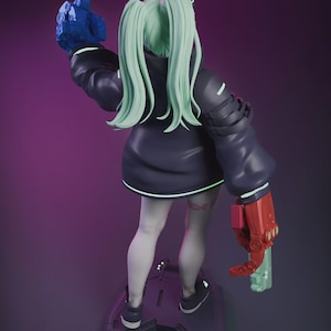 May include: A futuristic figurine of a female character with mint green hair in pigtails, wearing a dark blue jacket and white leggings. The figure has robotic arms, one blue and one red, and is standing on a gray platform. The background is a gradient of purple.