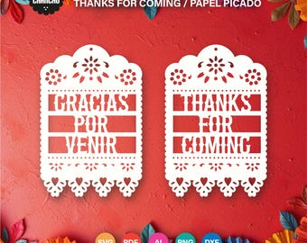 May include: Two white paper cut-out tags with the phrases "GRACIAS POR VENIR" and "THANKS FOR COMING" in a decorative font. The tags have a scalloped edge and floral cut-out details. The background is red with colorful paper fan decorations.