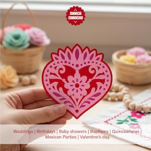 May include: A red and pink heart-shaped paper cutout with a floral design. The cutout is held in front of a blurred background with baskets of flowers and the text "Weddings | Birthdays | Baby showers | Baptisms | Quincea&ntilde;eras | Mexican Parties | Valentine's day."