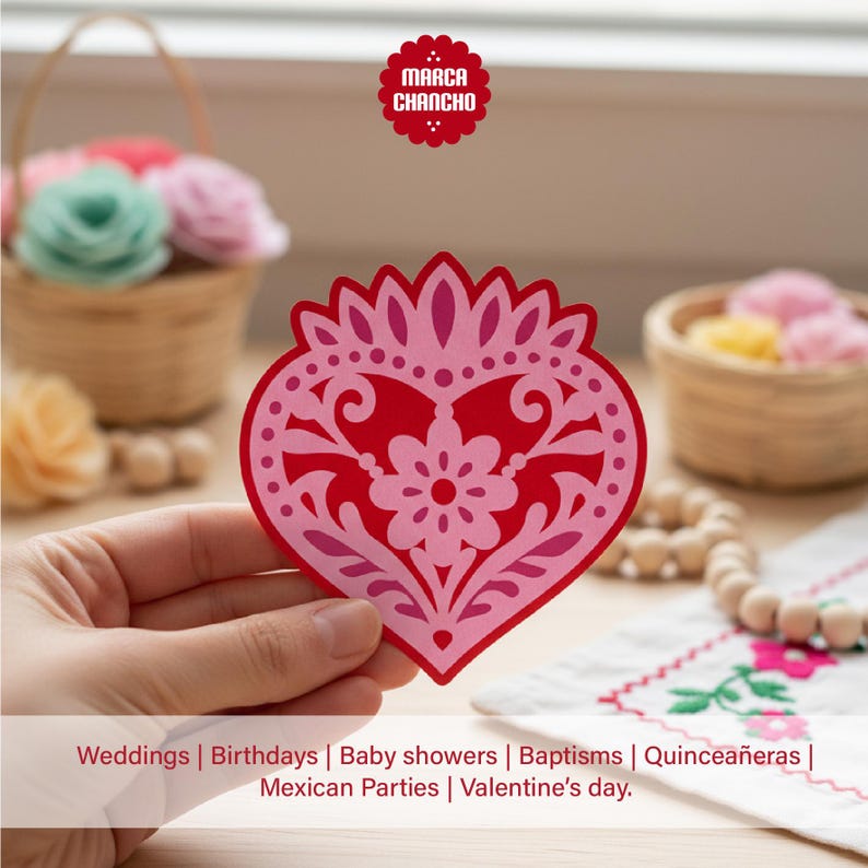 May include: A red and pink heart-shaped paper cutout with a floral design. The cutout is held in front of a blurred background with baskets of flowers and the text "Weddings | Birthdays | Baby showers | Baptisms | Quincea&ntilde;eras | Mexican Parties | Valentine's day."