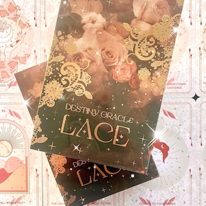 Puede incluir: Un primer plano de una baraja de cartas de oráculo llamada "Destiny Oracle Lace". Las cartas presentan un diseño floral con encaje dorado y una combinación de colores rosa y marrón. El texto "Destiny Oracle Lace" está impreso en dorado en la parte delantera de las cartas.