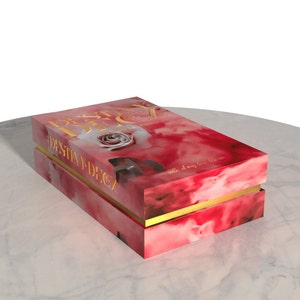 Peut inclure: Une bo&icirc;te rouge avec une bordure dor&eacute;e et une rose blanche sur le devant. La bo&icirc;te porte l'inscription "Destiny Deck" en lettres dor&eacute;es sur le devant. La bo&icirc;te est pos&eacute;e sur une surface en marbre blanc.