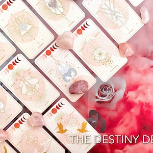 Könnte beinhalten: Ein Tarotkartenspiel mit dem Titel "The Destiny Deck" mit einem hellrosa und goldenen Design. Die Karten zeigen himmlische Illustrationen und sind mit Rosenquarz-Kristallen angeordnet. Der Hintergrund ist ein weiches rosa Blumenmuster.