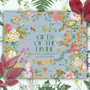 May include: A blue book with a floral design and the title "Gifts of the Divine: A Tarot Guidebook by Lisa Sanitine".