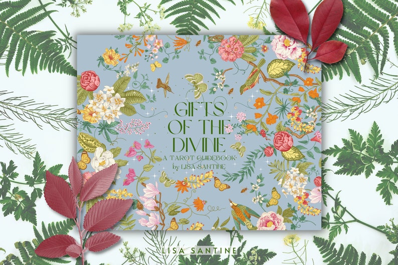 May include: A blue book with a floral design and the title "Gifts of the Divine: A Tarot Guidebook by Lisa Sanitine".