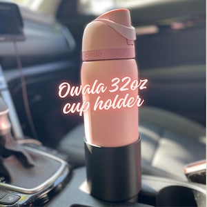 May include: A pink Owala 32oz cup holder, with a black cup holder base, sits in a car. The cup has a pink lid and a white handle. The text "Owala 32oz cup holder" is written on the cup.