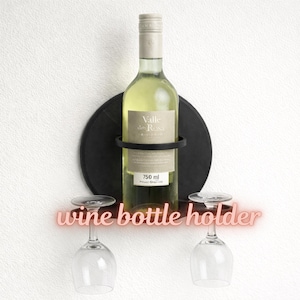 Può includere: Un portabottiglie nero con schienale rotondo, che contiene una bottiglia di vino bianco. Due calici sono appesi sotto. Il testo "wine bottle holder" è in neon rosa. La bottiglia di vino è da 750 ml.