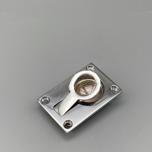 May include: A polished silver recessed pull with a rectangular base and a circular handle. The handle is attached to a pivoting arm that retracts into the base. Four screw holes are visible in each corner of the base.