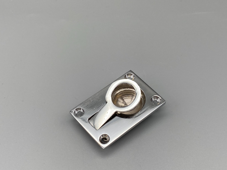 K&ouml;nnte beinhalten: Ein polierter, versenkter Griff aus Silber mit rechteckiger Basis und rundem Griff. Der Griff ist an einem schwenkbaren Arm befestigt, der sich in die Basis zur&uuml;ckzieht. Vier Schraubenl&ouml;cher sind in jeder Ecke der Basis sichtbar.