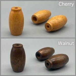 Puede incluir: Tiradores de cajón de madera en acabados de cerezo y nogal. Los tiradores de cerezo son de color marrón claro, mientras que los tiradores de nogal son de color marrón oscuro. Los tiradores tienen forma cilíndrica con un agujero en el centro. Se muestran las palabras "Cherry" y "Walnut".
