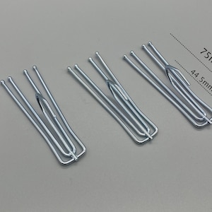 May include: Three silver curtain hooks. Each hook is made of thin, curved metal rods. The hooks are approximately 3 inches long and 1.75 inches wide. The hooks are designed to hold curtains.