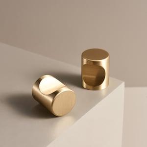 Puede incluir: Dos tiradores cilíndricos de latón dorado con un diseño de asa curvada. Los tiradores son de color dorado cálido y se encuentran sobre una superficie de tonos neutros. Están diseñados para un agarre fácil y añaden elegancia a cualquier mueble.