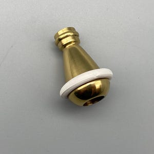 May include: A brass-colored, conical object with a white ring around its base. The object has a rounded bottom and a threaded top. The item is likely a decorative or functional component, possibly for furniture or a similar application.