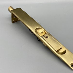 Peut inclure: Un pêne dormant en laiton avec un corps rectangulaire et une extrémité arrondie. Le pêne dormant est doté d'un mécanisme coulissant et d'une petite poignée circulaire. Conçu pour être installé à fleur d'une porte ou d'une autre surface.