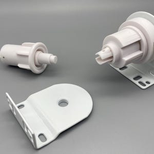 May include: White roller shade hardware components, including a roller tube end, a bracket, and a clutch mechanism. The components are made of plastic and metal, designed for window coverings. The parts are shown on a gray background.