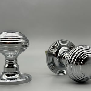 May include: Two shiny chrome door knobs with a ribbed design. One knob is upright, showing the base and stem, while the other is lying on its side. The knobs have a classic, vintage aesthetic.