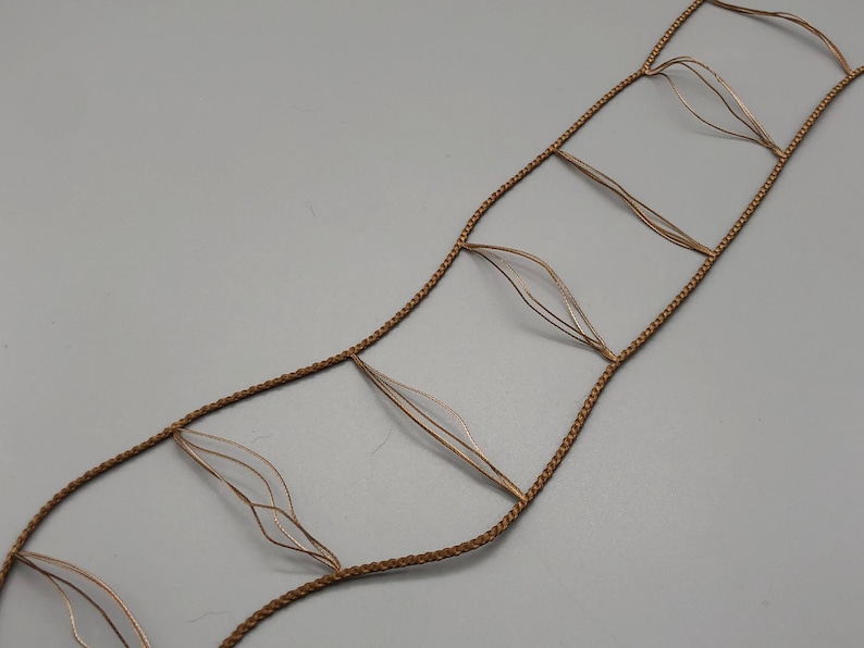 May include: A decorative, openwork design featuring a series of interconnected, leaf-shaped elements. The design is constructed from a light brown, braided cord, with delicate, translucent, leaf-like accents. The overall aesthetic is delicate and airy.