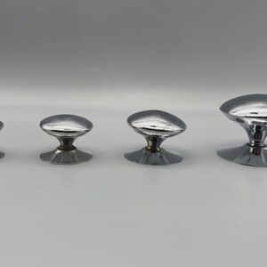 May include: Four shiny, chrome-finished cabinet knobs of varying sizes are arranged in a row. Each knob features a rounded, oval-shaped top and a flared base. The knobs are designed for furniture or cabinetry.