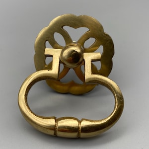 Könnte beinhalten: Ein Messing-Schubladengriff mit dekorativer floraler Rückplatte und rundem Griff. Die Hardware hat eine helle, polierte Oberfläche und das Design ist von Vintage inspiriert. Der Griff ist für Schränke, Schubladen oder Möbel geeignet.