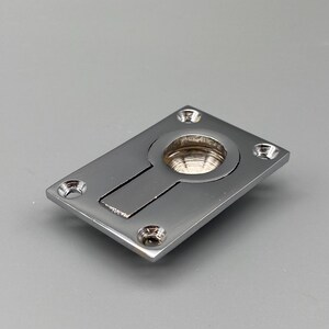 K&ouml;nnte beinhalten: Ein polierter, verchromter Einbaugriff mit rechteckiger Platte und rundem Zug. Der Griff hat einen rechteckigen Schlitz und vier Schraubenl&ouml;cher. Die Hardware ist f&uuml;r eine b&uuml;ndige Montage konzipiert.