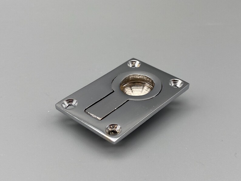 K&ouml;nnte beinhalten: Ein polierter, verchromter Einbaugriff mit rechteckiger Platte und rundem Zug. Der Griff hat einen rechteckigen Schlitz und vier Schraubenl&ouml;cher. Die Hardware ist f&uuml;r eine b&uuml;ndige Montage konzipiert.