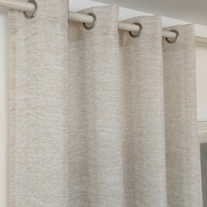 May include: Beige linen-textured curtain panels with silver eyelets. The curtains are hanging on a white rail. The fabric has a subtle, natural weave, creating a soft, neutral backdrop. The curtains are closed.