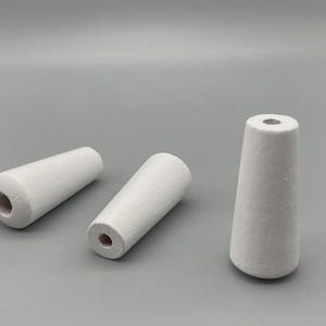 Könnte beinhalten: Drei weiße, kegelförmige Objekte mit strukturierter Oberfläche. Jedes hat oben und unten ein Loch. Die Objekte sind auf grauem Hintergrund angeordnet.