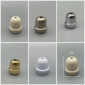 May include: A collection of six decorative, small, rounded finials in various metallic finishes. The finials are approximately 0.7 inches tall and 0.7 inches wide. Finishes include white, silver, gold, and a brushed metal look. Each has a small hole at the top.