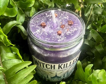 May include: A jar candle with a purple wax and a white wick. The candle is decorated with small brown pieces and white specks. The label reads "Witch Killer" with a church silhouette.