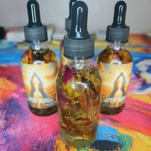 May include: Four glass dropper bottles filled with a golden liquid and botanical elements. Each bottle has a black cap and a label with the words "OPEN ROADS" and an illustration. The bottles are on a colorful, patterned surface.