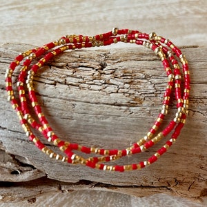 May include: A red and gold beaded bracelet with multiple strands of beads. The bracelet is made with small, round beads.