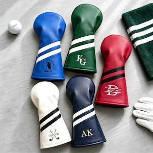 Könnte beinhalten: Fünf Golfschlägerhauben in Blau, Grün, Rot, Weiß und Marineblau, jeweils mit zwei Streifen und personalisierter Stickerei. Die blaue Haube zeigt Jack, die grüne KG, die rote Dylan, die weiße Oliver und die marineblaue AK.