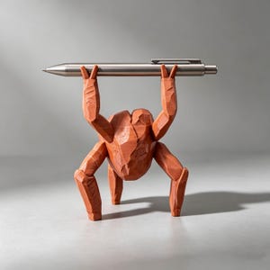 May include: A terracotta-colored, faceted figurine shaped like a four-legged creature with raised arms holding a silver metallic pen horizontally. The sculpture features sharp, angular planes and a matte finish, supporting the pen above its head.