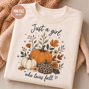 Puede incluir: Una sudadera de cuello redondo color crema con un estampado gráfico que incluye el texto "Just a girl who loves fall". El diseño muestra tres calabazas, una naranja, una blanca y una con estampado de leopardo, rodeadas de hojas y flores otoñales.