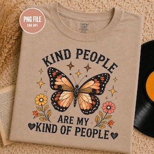 Puede incluir: Una camiseta color canela con un gráfico central de mariposa monarca rodeado de pequeñas estrellas, dos flores y el texto "KIND PEOPLE ARE MY KIND OF PEOPLE" en fuente marrón oscuro. La camiseta tiene cuello redondo y etiqueta de marca.