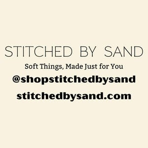 Pu&ograve; includere: Sfondo color crema con il testo "STITCHED BY SAND" in nero, con un carattere elegante. Sotto, si legge "Soft Things, Made Just for You". Vengono visualizzati anche l'handle di Instagram "@shopstitchedbysand" e il sito web "stitchedbysand.com".