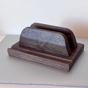 May include: A dark brown wooden desk organiser with a rectangular base and two arched dividers. The organiser is made of solid wood and has a smooth, polished finish. The design is simple and modern, suitable for holding mail or documents.