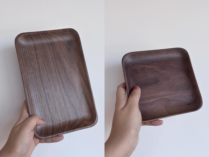 May include: Two images of a rectangular wooden tray with rounded corners. The tray is a dark brown color with visible wood grain. One image shows the tray held in a hand, and the other shows the tray on its own.