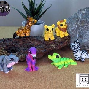 Op de afbeelding: Een verzameling kleurrijke 3D-geprinte dierenfiguren, waaronder een giraffe, een leeuw, een zebra, een krokodil, een nijlpaard en een vogel. De giraffe is geel en bruin, de leeuw is geel met een bruine manen en de zebra is zwart en wit.