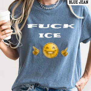 May include: Blue jean-coloured t-shirt featuring the text "FUCK ICE" in white block letters. Below the text is a yellow emoji with a smiling face and two finger-pointing emojis. The shirt has a casual style.