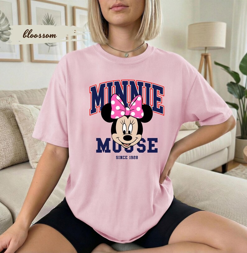 May include: A pale pink t-shirt with a Minnie Mouse graphic. The design includes a pink polka dot bow and the text "MINNIE MOUSE" above the character, with "SINCE 1928" below. The shirt has a relaxed fit.