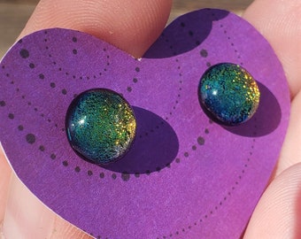 May include: A pair of iridescent glass earrings with a green, gold, and blue colour scheme. The earrings are round and have a speckled texture.