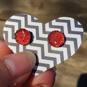 May include: A pair of red rhinestone stud earrings displayed on a black and white chevron patterned heart-shaped card.