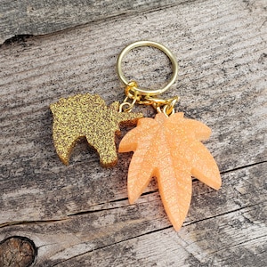 May include: Gold and orange glitter resin keychain with a leaf and a small animal shape.