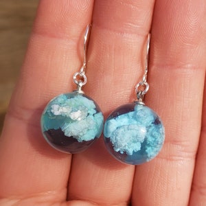 Pendientes de resina Nubes y Cielo Azul: Esfera de resina de cielo azul brillante y soleado con esponjosas nubes blancas en su interior, engarzada en alambres rellenos de plata de ley.